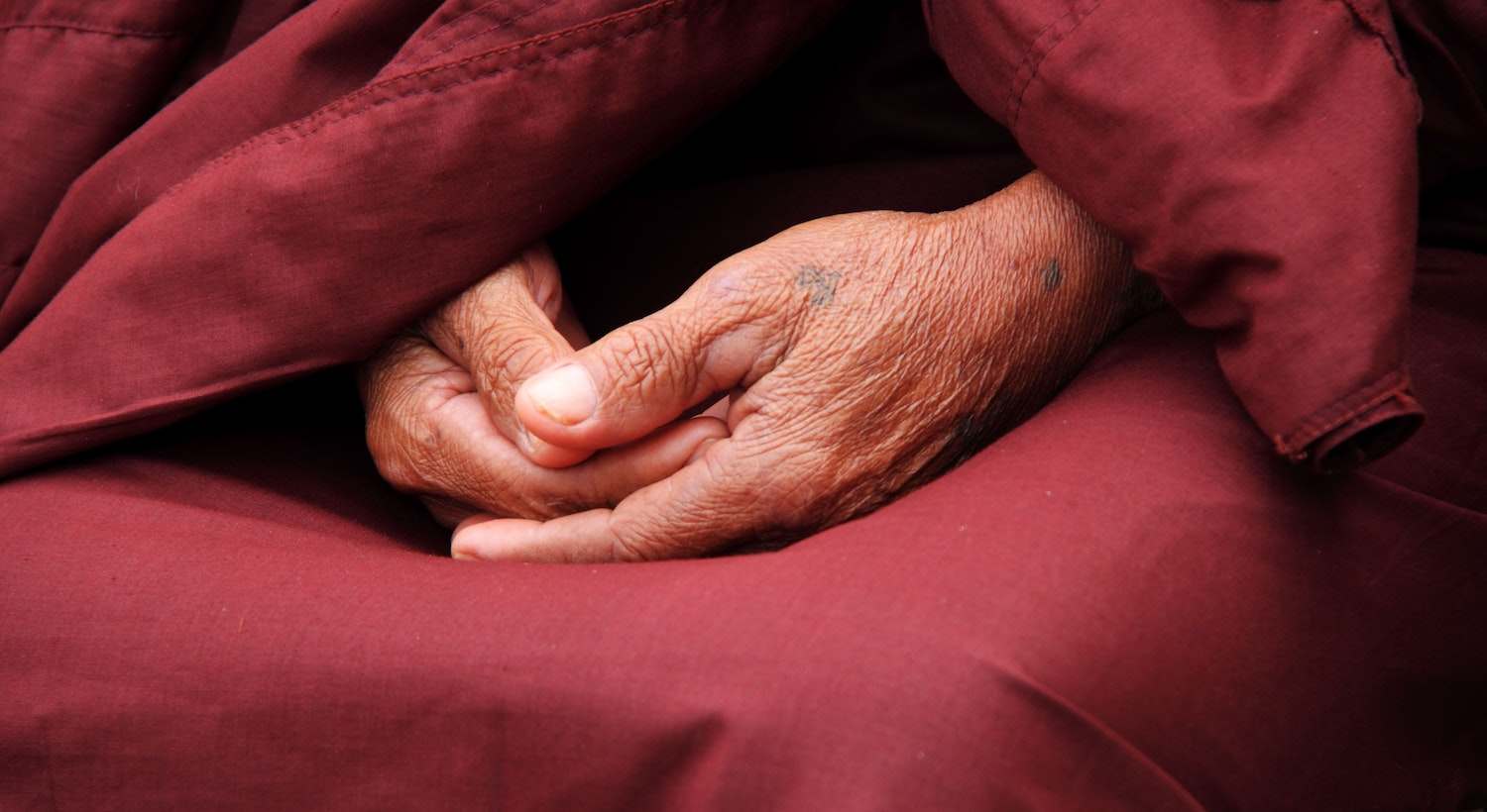 homem sentado com as mãos encostadas fazendo Reflexões Budistas com a roupa vermelha própria