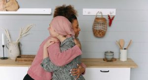 em uma cozinha, uma mulher negra está abraçando uma mulher branca, refletindo sobre Se Colocar No Lugar Do Outro em vários momentos da vida