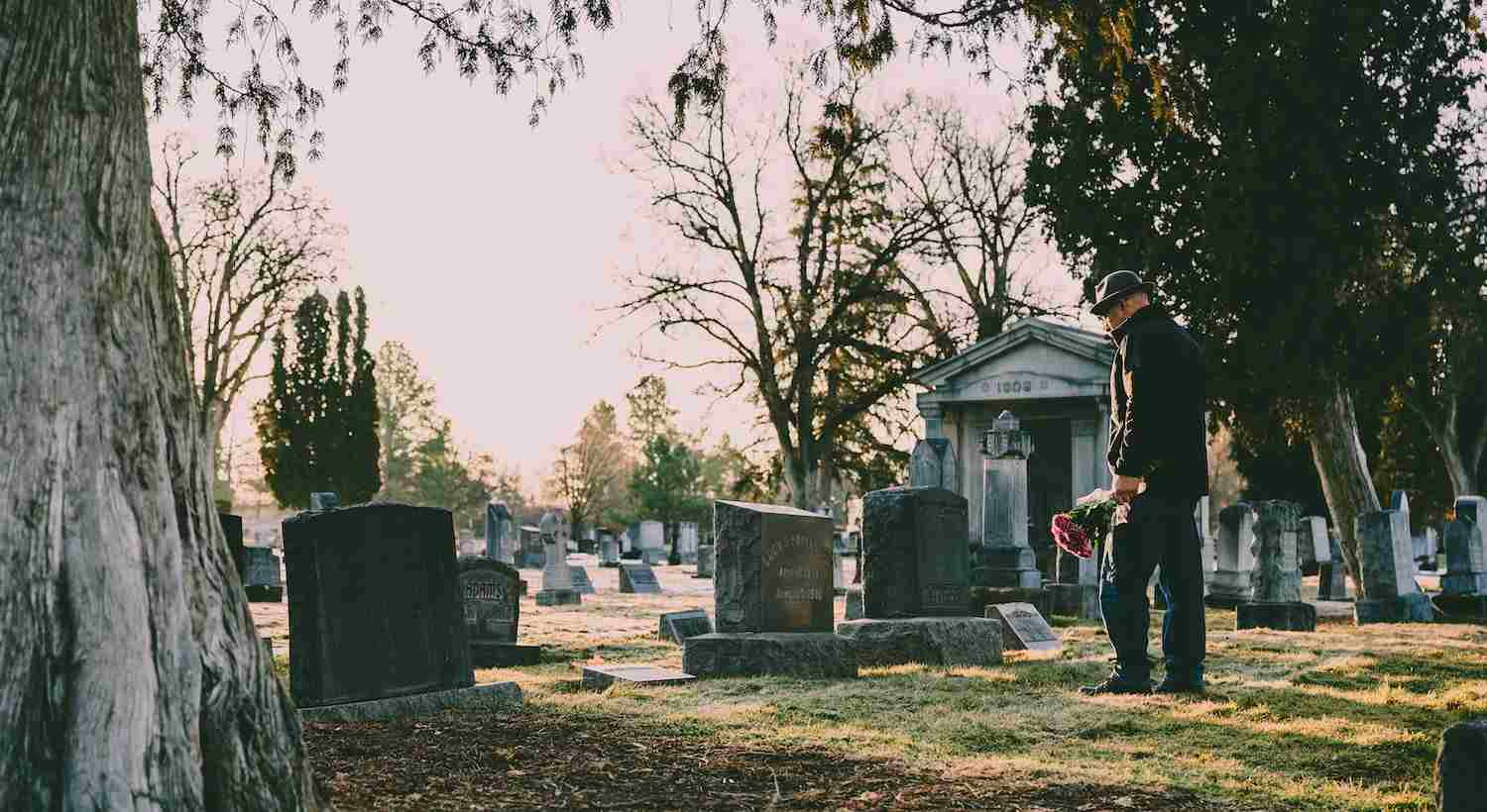 um homem visitando o cemitério, com flor no túmulo se perguntando O Que Acontece Depois da Morte Segundo o Espiritismo
