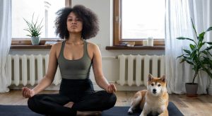 mulher negra sentada em posição de lótus fazendo Aula de Yoga Online ao lado do seu cachorro