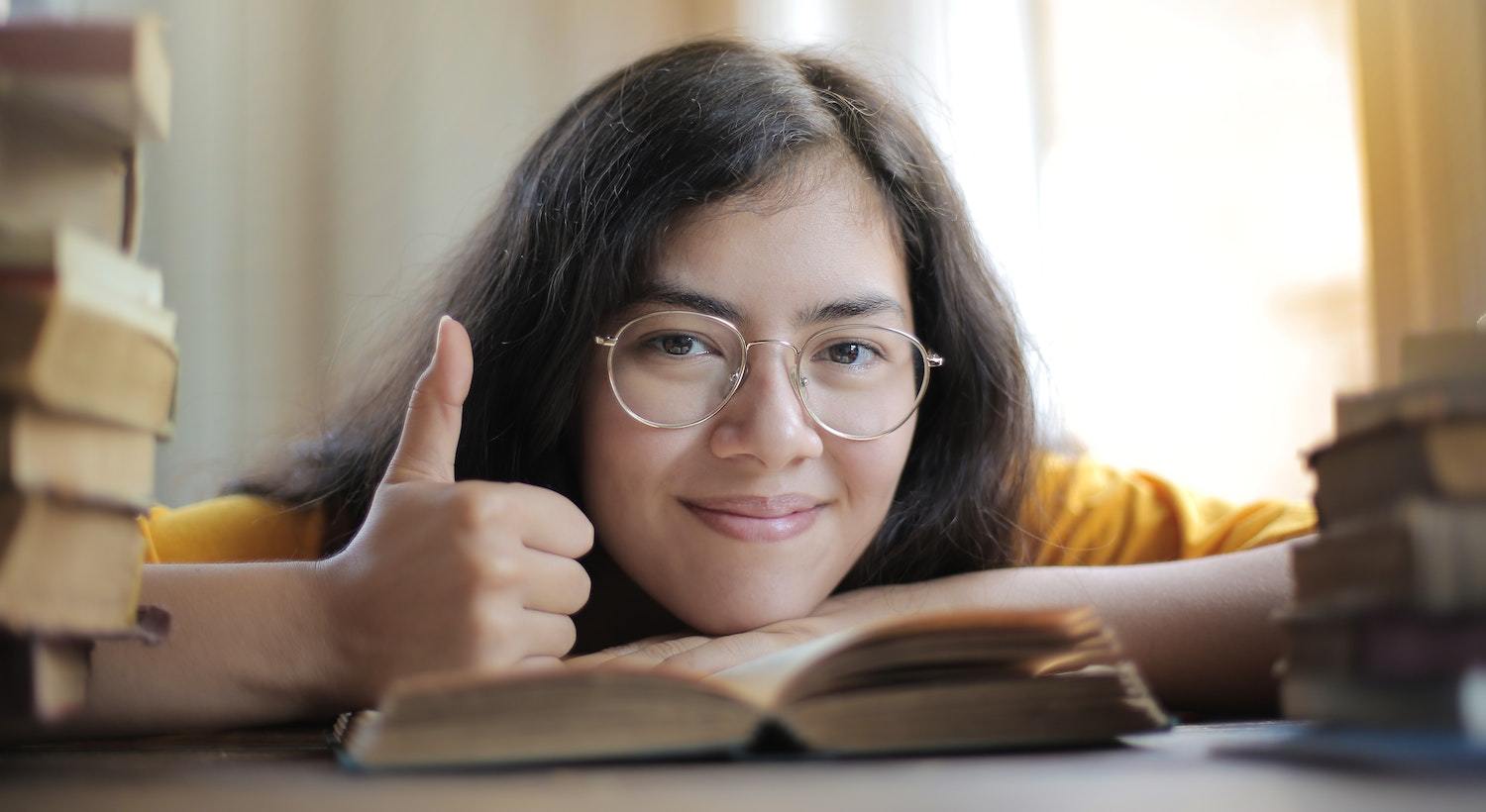 mulher fazendo sinal de positivo com a mão, de frente a um livro sobre Auto estima e Amor Próprio