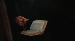 uma pessoa segurando a bíblia e o rosário meditando em como ser uma pessoa melhor para Deus