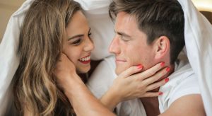 um casal sorrindo olhando um para o outro na cama simbolizando o que acontece espiritualmente quando duas pessoas fazem amor